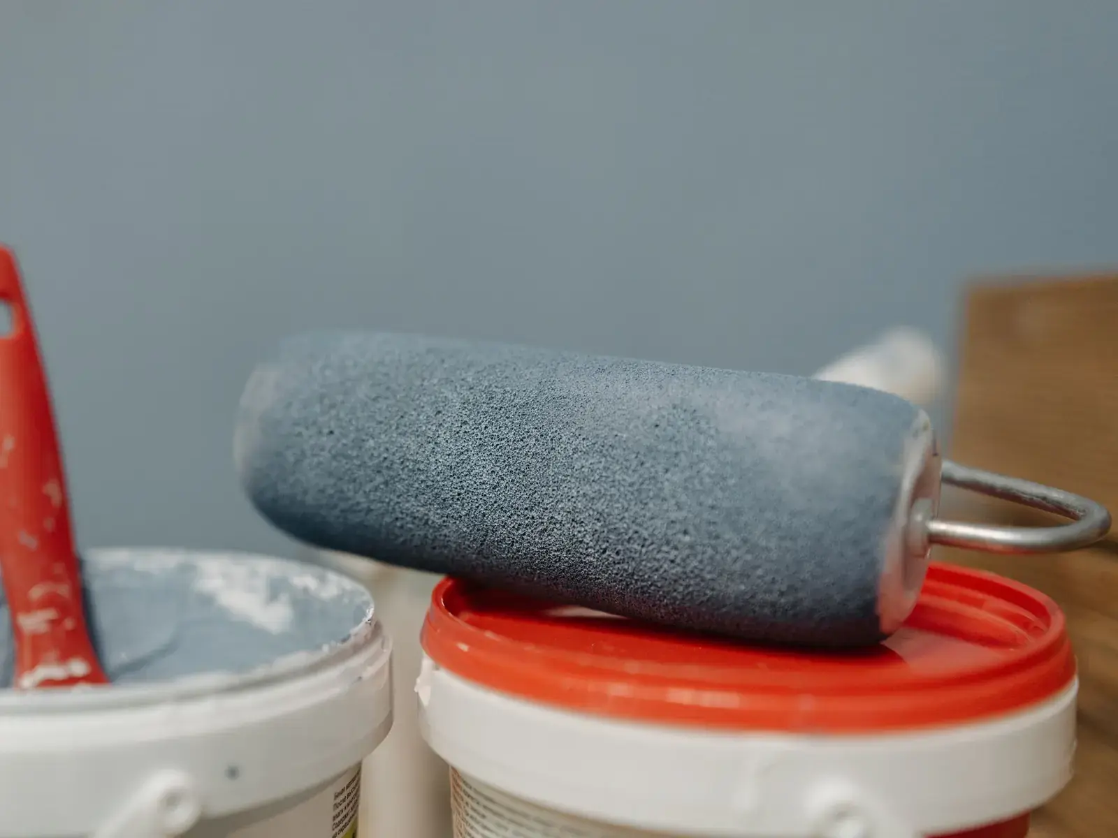 A roller loaded with grey coating resting on open pails of waterproof coating