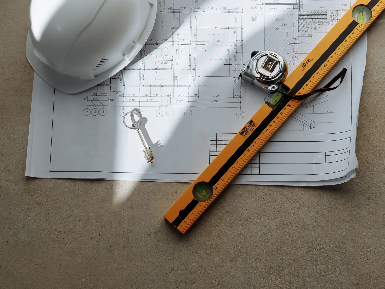 A hard hat, measuring tape, folding ruler and keys resting on a set of building plans